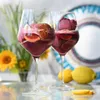 Two glasses of red wine slushy with fruit garnishes, lemons, and flowers in the background. Produktbild-Vorschau