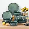 A collection of green stoneware tableware is arranged on a wooden surface, with lemons, a pepper grinder, and a vase of yellow flowers as props. Voir les images du produit