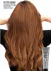 A person's back with long, wavy, reddish-brown hair is shown, with a product tube in the lower right corner. Náhled obrázku produktu