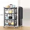 A black four-tier kitchen cart with various kitchen appliances and containers on its shelves, shown in a room with a tiled wall. Produktbild-Vorschau
