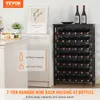 A black wine rack filled with wine bottles, placed next to a white cabinet with a framed picture and some cupcakes on top. There is also a decanter and two wine bottles on top of the wine rack. Náhľad obrázku produktu