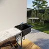 An outdoor sink area with a marble countertop and a black sink, set against a white wall, with a garden and patio in the background. Produktbild-Vorschau