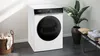 A Siemens washing machine is shown in a laundry room setting with a basket of clothes and a plant. Produktbild-Vorschau