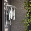 A white wall-mounted drying rack with clothes hanging on it, set against a brick wall. Produktbild-Vorschau