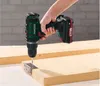 A hand is using a cordless drill to screw a hinge onto a piece of wood. Produktbild-Vorschau