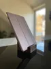 A tablet case is propped up on a wooden stand on a reflective surface, with a blurred background of a window and trees. Produktbild-Vorschau