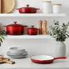 A collection of red cast iron cookware and kitchen accessories displayed on white shelves and a countertop. Anteprima dell’immagine prodotto