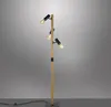 A modern floor lamp with a wooden pole and three adjustable black spotlights. Produktbild-Vorschau