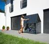 A woman is opening a metal storage box for bicycles next to a modern house. Náhľad obrázku produktu