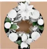 A Christmas wreath with white poinsettias, silver pine needles, and white baubles, set against a brown cardboard background. Anteprima dell’immagine prodotto