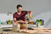 A man is using a cordless drill to assemble a wooden box in a workshop. Produktbild-Vorschau