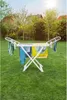 A white clothes drying rack with laundry is set up on a green lawn in a backyard with trees and houses in the background. Náhled obrázku produktu