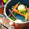 A close-up shot of a copper pot filled with fresh vegetables, including carrots, broccoli, and cauliflower, placed on a wooden surface. Produktbild-Vorschau