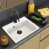 A kitchen sink with a faucet running water, a dish rack with cucumbers, and a knife block. Podgląd zdjęcia produktu