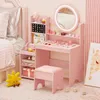A pink children's vanity set with a mirror, shelves, and stool, placed in a bedroom setting. Voir les images du produit