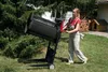 A woman is operating a large cylindrical screening machine in a grassy yard with trees and a stack of firewood in the background. Náhľad obrázku produktu
