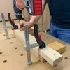 A person is using a cordless drill to screw into a piece of wood that is clamped to another piece of wood. Náhľad obrázku produktu