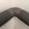 A close-up view of a 90-degree pipe insulation elbow with clips, attached to a wall. Produktbild-Vorschau