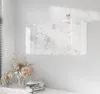 A wall-mounted bathroom cabinet with a marble-effect front is shown against a white wall. A vase of dried flowers and folded towels are on a shelf below. Produktbild-Vorschau