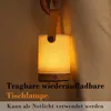 A hand holds a portable LED table lamp with a wooden base and fabric shade, casting a warm glow. Produktbild-Vorschau