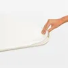A hand is shown tucking a white fabric over the edge of a beige ironing board cover. Produktbild-Vorschau