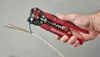 A hand is holding a wire stripper tool and is in the process of stripping a wire. Produktbild-Vorschau