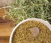 A close-up view of animal feed pellets in a white bucket, with hay scattered on a wooden surface. Produktbild-Vorschau