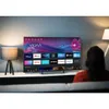 A person is sitting on a couch watching a smart TV in a living room setting. Produktbild-Vorschau