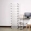 A tall, white, multi-compartment storage unit stands against a white wall, next to a desk with a computer monitor and a small drawer unit. Produktbild-Vorschau