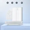 A white UGREEN smartphone wall mount is displayed on a light blue surface, with a pile of white pellets cascading down from the top left. Produktbild-Vorschau