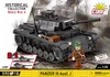 A COBI building block set of a Panzer III Ausf. J tank, with a soldier figure, set against a blurred background of a war-torn environment. Náhľad obrázku produktu