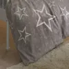 A close-up view of taupe bedding with white stars, placed on a wooden floor next to a white crib and a cream rug. Produktbild-Vorschau