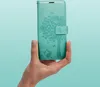 A hand holds a teal-colored phone case with a tree and butterfly design against a light teal background. Náhled obrázku produktu