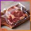 Two vacuum-sealed raw steaks on a wooden cutting board. Podgląd zdjęcia produktu