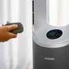 A hand holding a remote control near a modern tower fan. Podgląd zdjęcia produktu