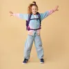 A young girl with a backpack and a colorful cardigan is posing with her arms outstretched. Náhled obrázku produktu