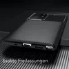A close-up shot of a black smartphone case with a carbon fiber texture, placed on a dark, ribbed surface. Produktbild-Vorschau