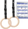 Two wooden gymnastic rings with black adjustable straps are shown hanging, with a poster of exercises in the background. Produktbild-Vorschau