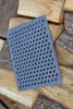 A gray cast iron grate with many holes rests on a pile of chopped wood. Produktbild-Vorschau