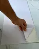 A hand is peeling the backing off a white textured panel with a marble-like surface. Produktbild-Vorschau