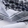 A close-up view of a folded black and white patterned scarf. Produktbild-Vorschau