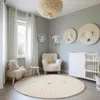 A nursery room with a crib, armchair, and a round rug. Produktbild-Vorschau