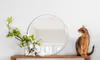 A round mirror with a white frame sits on a wooden shelf next to a vase of flowers and a cat. Produktbild-Vorschau