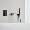 A black built-in bathtub faucet with a waterfall spout and a handheld showerhead is mounted on a white wall above a white bathtub. Podgląd zdjęcia produktu