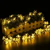 A string of flower-shaped lights illuminates a planter box with a white picket fence. Produktbild-Vorschau