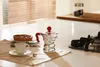 A coffee maker, cup, and tart are arranged on a kitchen counter. Produktbild-Vorschau