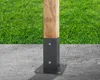 A wooden post is secured to a concrete surface by a metal base and bracket. Green grass is visible in the background. Náhled obrázku produktu