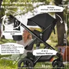 A woman is sitting behind a stroller in an outdoor setting. Produktbild-Vorschau