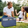 A family having a picnic in a park with a picnic basket in the foreground. Voir les images du produit