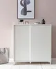 A white shoe cabinet with sliding doors is shown in a room with a pink wall and a framed abstract picture above it. A grey tote bag is placed on the floor to the left of the cabinet. Náhled obrázku produktu